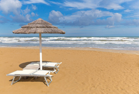 在阳光明媚的日子, 海边有椅子的沙滩伞。里米尼海岸线。意大利度假村。在海滩背景上复制空间