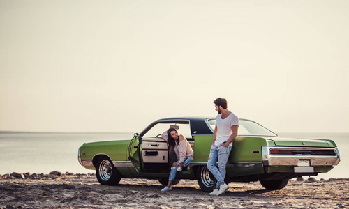 浪漫情侣站在海滩上的绿色复古汽车附近.