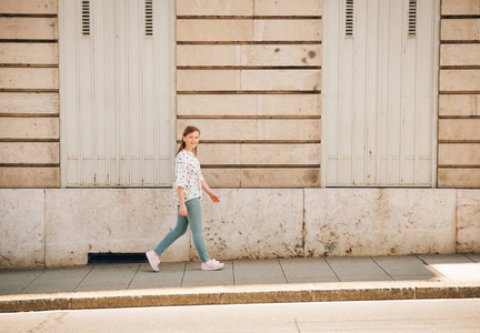 小女孩走在城市的街道上, 穿着衬衫, 蓝色长裤和粉红色运动鞋
