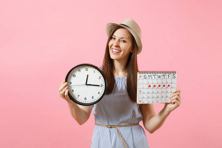 微笑的漂亮女人穿着蓝色的礼服, 戴着圆钟的帽子, 月经期的日历用来检查在粉红色背景下的经期。医疗保健妇科概念。复制空间