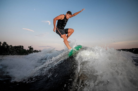 活跃和年轻人跳在 wakesurf 下河波浪对蓝色天空在日落