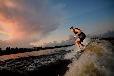 运动的人骑在 wakesurf 下河上的美丽的天空背景