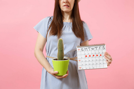 哀伤的妇女在蓝色礼服举行绿色仙人掌, 期间日历为检查在粉红色背景被隔绝的月经天。医疗, 医疗, 妇科, 胃痛的概念。复制空间