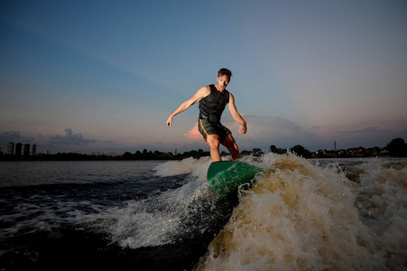 英俊的运动男子骑在 wakesurf 在美丽的天空在日落的背景下河