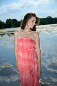 在波兰的户外摄影会上的年轻女性模特。女孩与长的红色礼服站立在湖附近