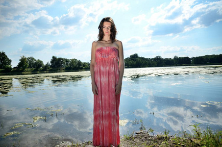 在波兰的户外摄影会上的年轻女性模特。女孩与长的红色礼服站立在湖附近