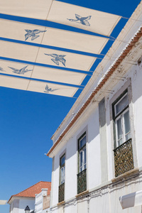 传统葡萄牙建筑的白色门面。屋顶的线与典型的瓷砖。有鸟的街荫。明亮的蓝天。维拉真正的圣安东尼奥, 阿尔加维, 葡萄牙