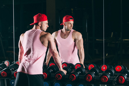 肌肉男了健身房站附近哑铃 粉红色衬衫，红色棒球帽