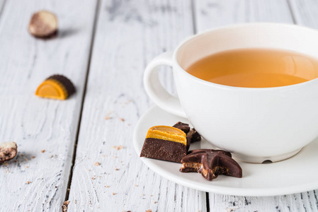 喝杯茶与原始手工巧克力糖果白色木制背景上。健康早餐与素食主义者糖果