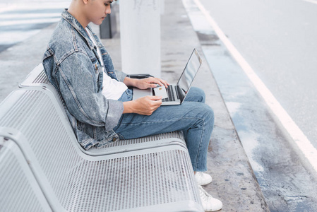 亚洲 hansome 的家伙正在工作的便携式计算机连接到公共无线网络, 而坐在椅子上的机场巴士站