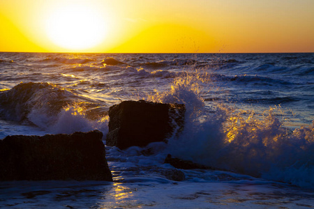 日落时美丽的大海。在黄色的太阳背景下喷洒和石头。海景