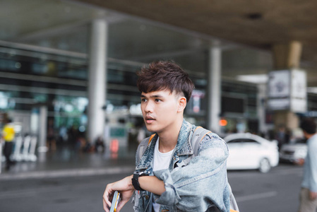 年轻的亚裔男子看着他的手表在机场候机楼前