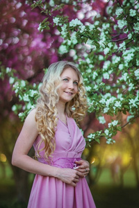 美丽的金发女孩与长发在一个盛开的花园粉红色的礼服