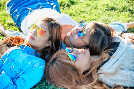 三个亚洲快乐女孩躺在绿草中的太阳镜
