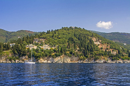 豪华白色帆船帆船在美丽的前面, 覆盖着绿树和别墅科孚岛, 希腊
