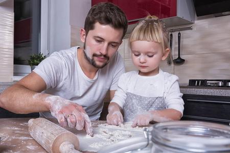 父亲节一个金发碧眼的小女孩花时间和她爸爸在厨房里做饭。假期的准备工作。烘烤