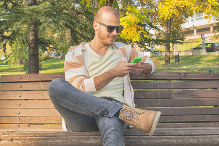 男子使用智能手机, 而坐在木凳上秋季公园