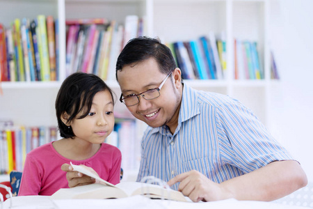 年轻教师的图片指导他的小学生读一本书, 而坐在图书馆