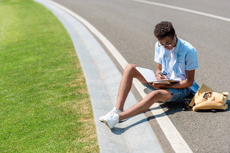 美国十几岁的黑人学生坐在滑板上的高角度视图和在公园看书