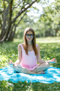 美丽的妇女沉思在绿色的草地上坐在莲花位置的公园。健身女孩锻炼后放松瑜伽姿势