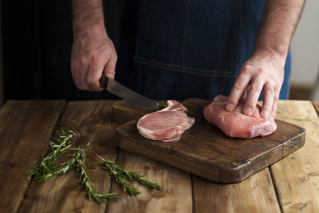 一个人在厨房围裙, 肉在木板和木桌, 迷迭香, 一把刀