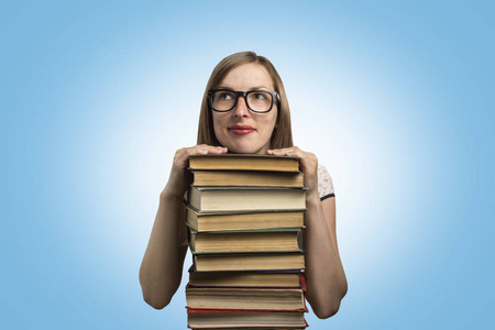 一个穿着白色连衣裙和眼镜的年轻女孩把手放在蓝色背景上的一堆书上。青年学生观念与教育