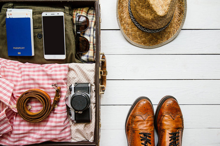 老式时髦的衣服, 鞋, 帽子, 智能手机, 配件包装在手提箱上的白色木桌。旅游理念。用于复制文本字体的空白空间