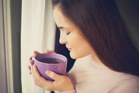 年轻女人在早上坐在窗边喝着茶