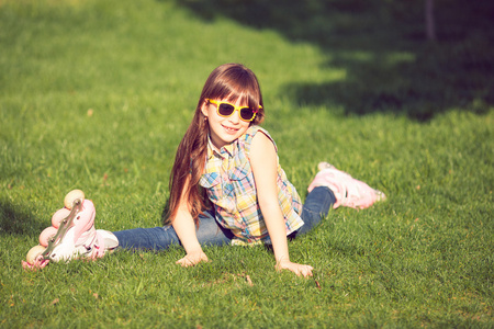 女孩穿着旱冰鞋坐在公园的草地上