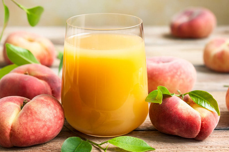 一杯新鲜桃汁包围新鲜水果与叶木桌上。健康早餐的概念