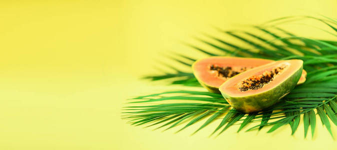 木瓜果在热带绿色棕榈叶上黄色的背景。复制空间。流行艺术设计, 创意夏日概念。纯素食的食物。旗帜