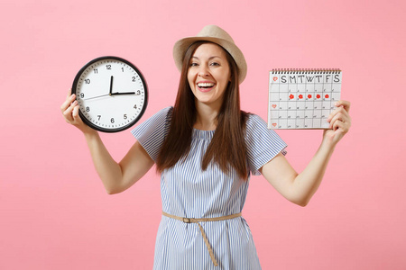 微笑的漂亮女人穿着蓝色的礼服, 戴着圆钟的帽子, 月经期的日历用来检查在粉红色背景下的经期。医疗保健妇科概念。复制空间