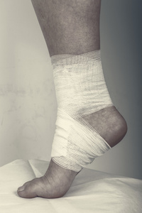 受伤的脚踝，用灰色的背景上的绷带