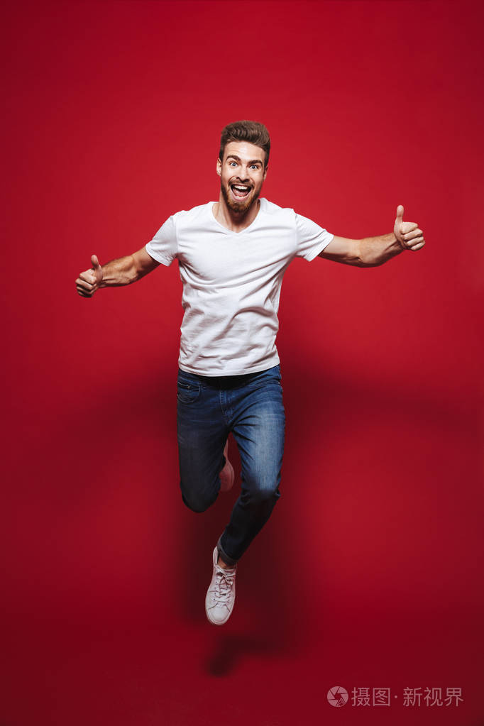 一个开朗的年轻胡子男子的全长肖像显示竖起大拇指, 而庆祝成功和跳跃孤立的红色背景