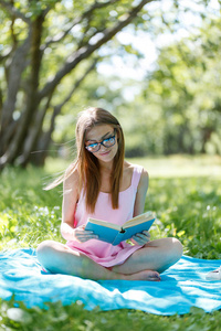 读一本书室外的年轻白人美女的画像。坐在草地上