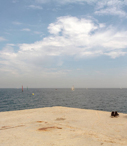 一对破旧的时髦运动鞋在海岸防波堤。西班牙巴塞罗那巴塞洛内塔海滩附近的地中海航行小船