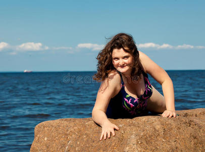 快乐的年轻女子躺在岩石上游泳。海滨
