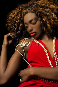 一位美丽的异国非洲裔美国妇女，穿着一件红色连衣裙，眼睛闭着，上面挂着珍珠