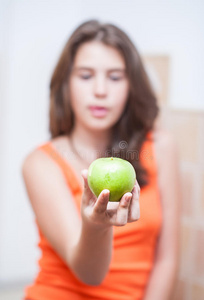 身穿橙色t恤的少女展示一个绿色苹果