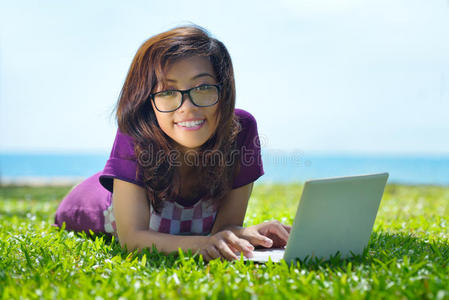 年轻的微笑学生在绿草地上玩笔记本电脑