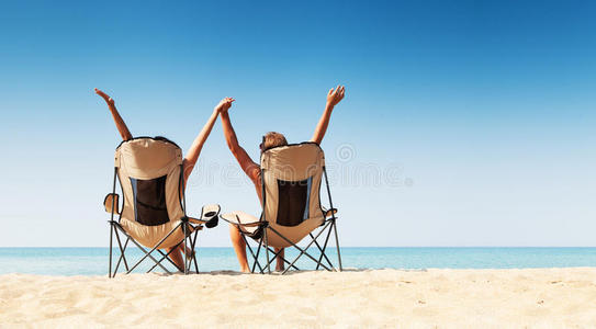 一对年轻夫妇坐在沙滩上舒适的椅子上