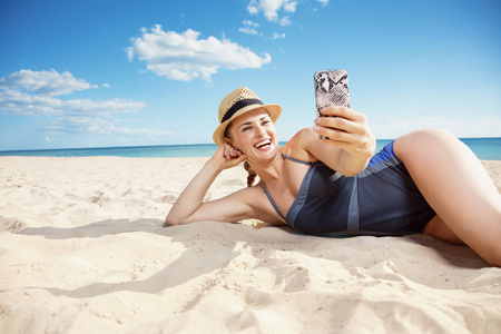 微笑的现代妇女在海滩采取自拍用移动电话在海岸