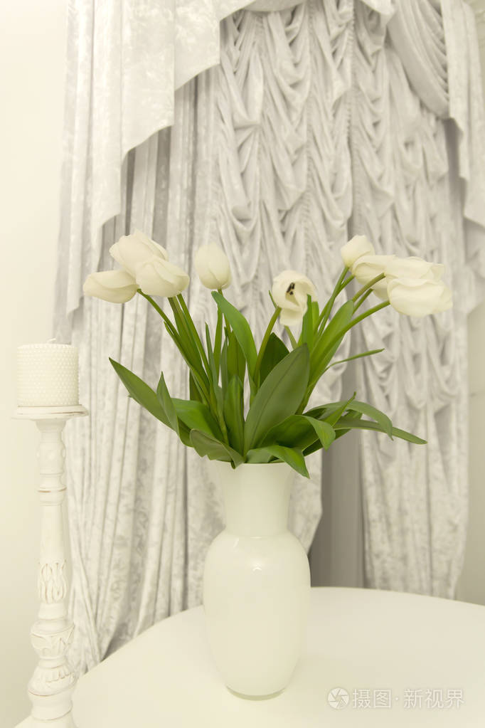 一束白色的郁金香在桌子上的花瓶在窗帘的背景上
