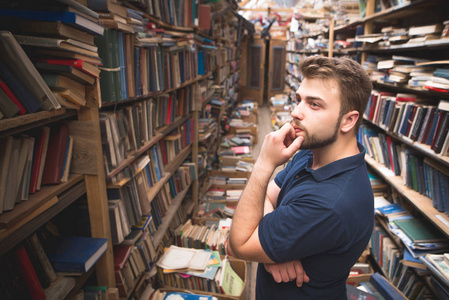 一个留有胡子的男人的肖像, 站在大气公共图书馆的背景上, 看着书架。学生在图书馆里选择书籍。公共图书馆文献检索