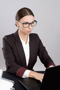 开朗的商业妇女坐在办公桌上, 文件和书籍, 并使用笔记本电脑