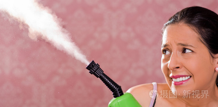 黑发女人抱着蒸汽清洁机和蒸汽出来吓人的面部表情，粉红色的背景