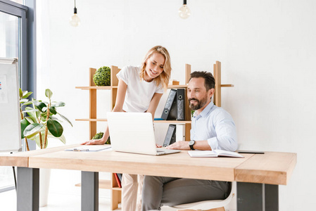 两个兴奋的同事讨论工作项目, 而坐在办公室和工作的笔记本电脑照片