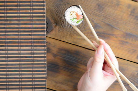 一只手拿着筷子在竹稻草 serwing 垫的背景上放上寿司卷。传统亚洲食品