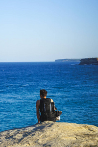 旅行者坐在悬崖边上, 望着海边漫步的蔚蓝海洋