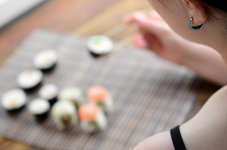 黑头发的女孩用筷子举行寿司卷在竹秸秆 serwing 垫背景。传统亚洲食品